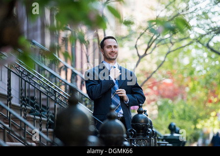 A man in a business suit adjusting his tie. At the bottom of the steps of a townhouse in a terrace. Stock Photo