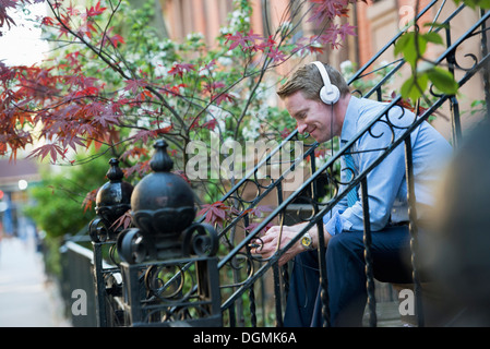 A man in a blue shirt wearing headphones and listening to a music player. Stock Photo