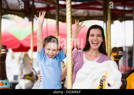 USA, Utah, Salt Lake City, Mother and son (4-5) on carousel in amusement park Stock Photo