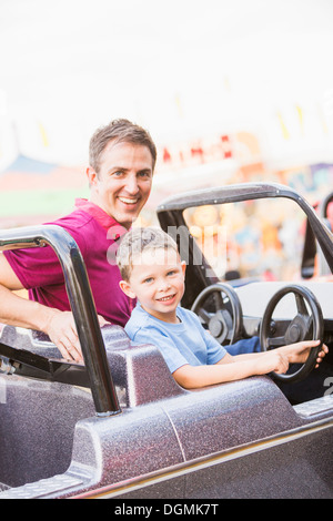 USA, Utah, Salt Lake City, Father with son (4-5) driving toy car in amusement park Stock Photo