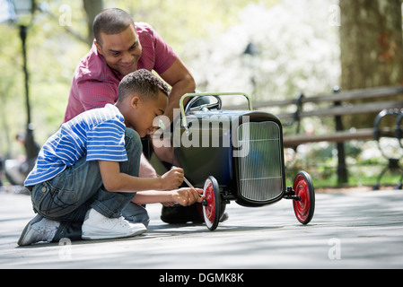 A boy repairing an old fashioned toy peddle car. Stock Photo