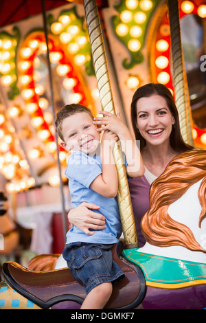 USA, Utah, Salt Lake City, Mother and son (4-5) on carousel in amusement park Stock Photo