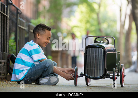 A young boy playing with a old fashioned toy car on wheels on a city street. Stock Photo