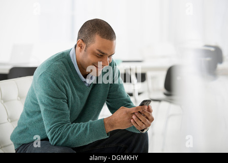 Business. A man seated, checking his smart phone for messages and texting. Stock Photo