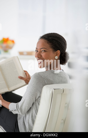Business. A woman sitting and reading a book. Research or relaxation. Looking over her shoulder and smiling. Stock Photo