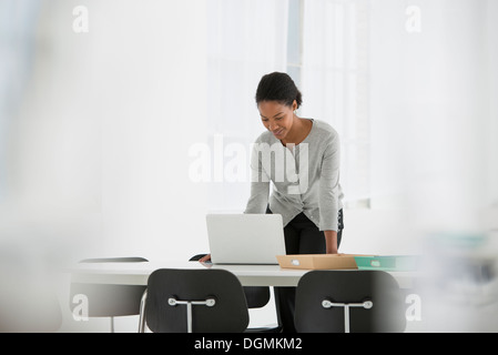 Business. A woman leaning over a desk using a laptop computer. Stock Photo