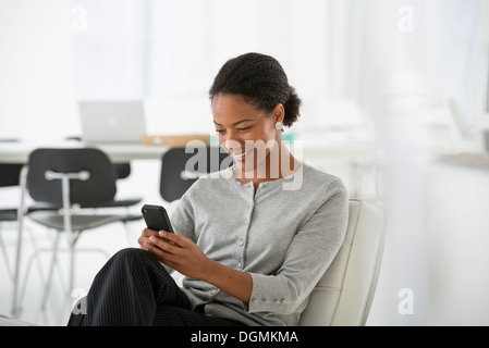 Business. A woman seated in a comfortable chair, checking her smart phone for messages. Stock Photo