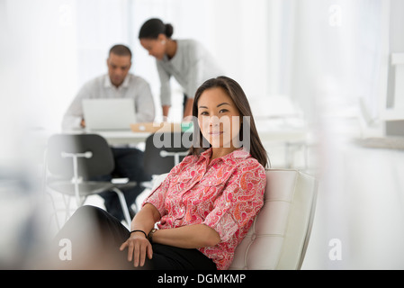 Business. A woman seated on the sofa looking relaxed. Two people working together looking at a laptop. Stock Photo