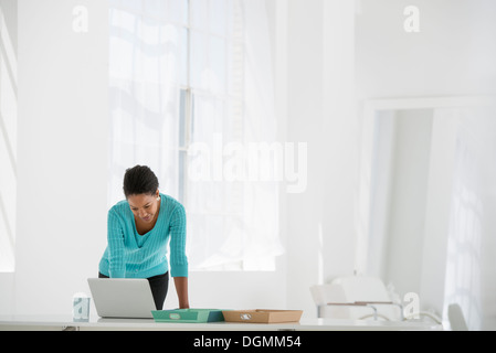 Business. A woman leaning over a desk using a laptop computer. Stock Photo