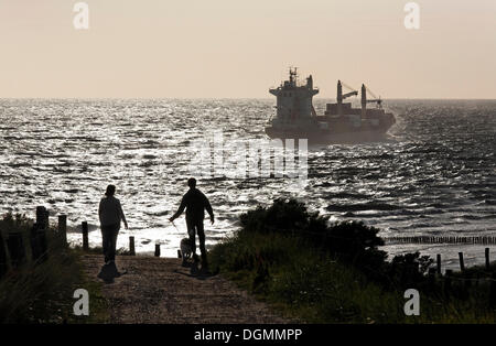 A couple taking a walk on the dunes, a cargo boat on the ocean, backlight, Zoutelande, Walcheren peninsula, Zeeland province Stock Photo