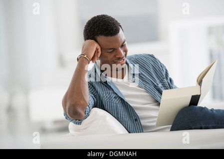 A bright white room interior. A man sitting reading a book. Stock Photo