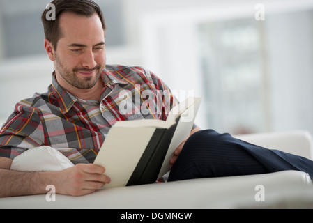 A bright white room interior. A man sitting reading a book. Stock Photo