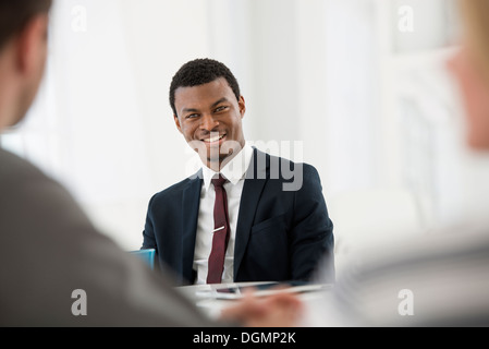 Office interior Three people sitting around table business meeting man in suit cup of coffee digital tablet on table. Stock Photo
