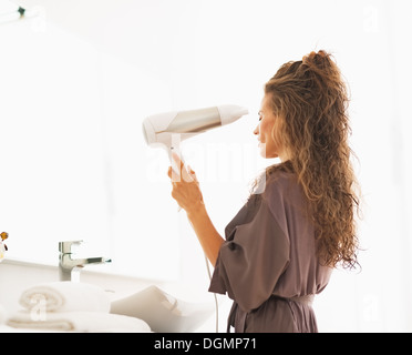 Young woman blow drying hair in bathroom Stock Photo
