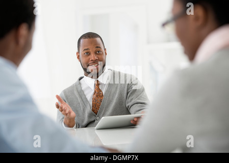 Office interior. Three people sitting around a table at a business meeting. Stock Photo