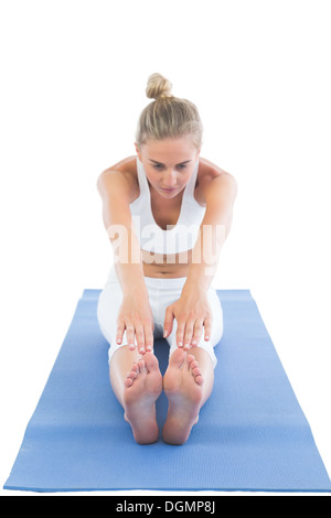 Toned focused blonde sitting on exercise mat stretching legs Stock Photo