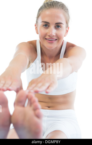 Toned happy blonde sitting on exercise mat stretching legs Stock Photo