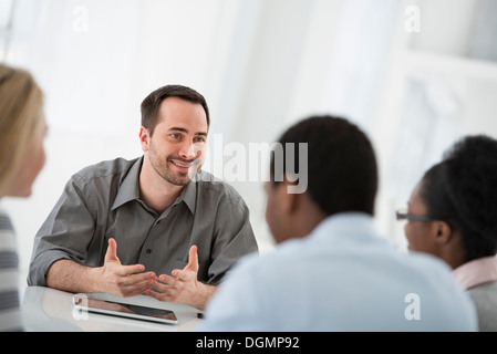 Office interior. A group of four people, two men and two women, seated around a table. Business meeting. Stock Photo