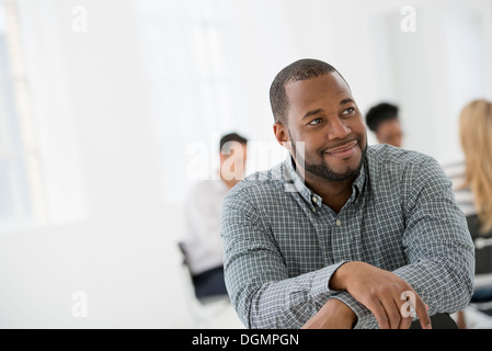 Office interior. A man seated separately from a group of people seated around a table. A business meeting. Stock Photo