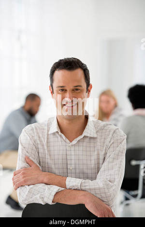 Office interior. A man seated separately from a group of people seated around a table. A business meeting. Stock Photo