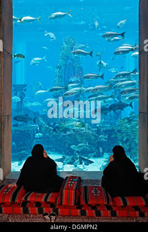 Two Arab women talking on their cell phones in front of an aquarium in The Lost Chambers, a theme park based on the legend of Stock Photo