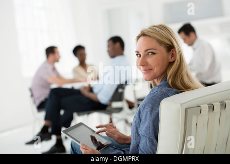 Office interior. Meeting. One person looking over her shoulder and away from the group. Holding a digital tablet. Stock Photo