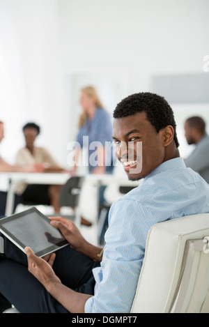 Office interior. Meeting. One person looking over his shoulder and away from the group. Holding a digital tablet. Stock Photo