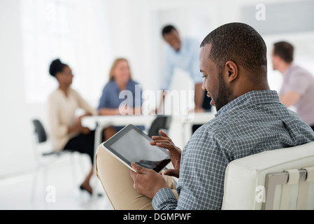 Office interior. Meeting. One person seated separately, using a tablet computer. Holding a digital tablet. Stock Photo