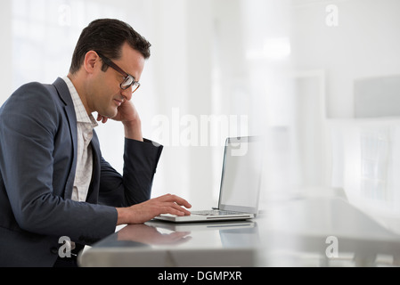 Office interior. A businessman seated at a table, using a laptop computer. Stock Photo