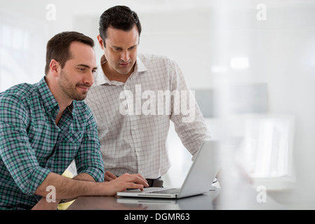 Office interior. Two men standing at a table using a laptop computer. Stock Photo