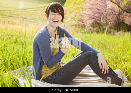 A young woman sitting in an open space, a grass field, on a blanket. Stock Photo
