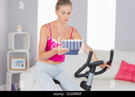 Sporty focused blonde training on exercise bike using tablet Stock Photo
