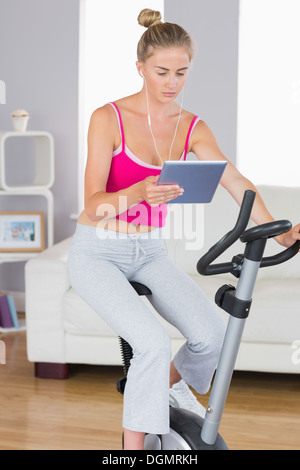 Sporty serious blonde training on exercise bike using tablet Stock Photo