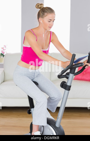 Sporty unsmiling blonde training on exercise bike using tablet Stock Photo