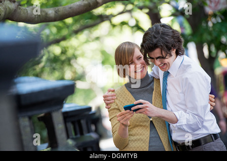 City. Two people, a man and woman outdoors, looking at a smart phone together. Stock Photo