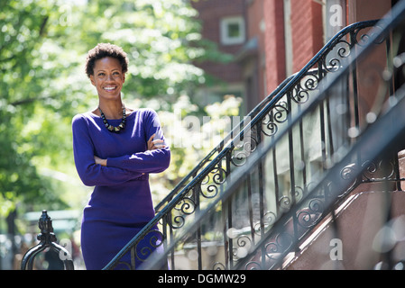 City. A woman wearing a purple dress, standing on the steps outside a townhouse. Stock Photo