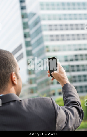 City. A man in a business suit holding his smart phone at arms length. Stock Photo