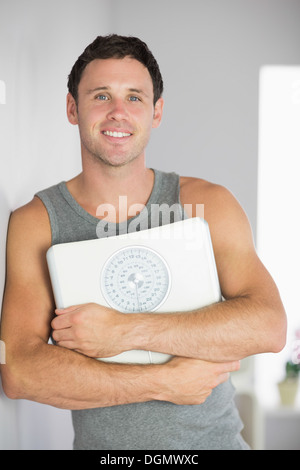 Sporty smiling man leaning against wall holding a scale Stock Photo