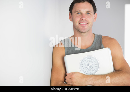 Sporty cheerful man leaning against wall holding a scale Stock Photo