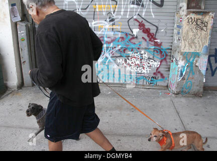 New York, New York, USA. 21st Oct, 2013. A man and his two dogs walk past British artist Banksy's graffiti art 'This is my New York Accent: normally I write like this' located on 10th Avenue and 25th Street in West Chelsea. This piece is part of the Banksy 'Better In Than Out' one month residency in NYC where a new work is installed once a day in one of the 5 boroughs in the city. © Nancy Kaszerman/ZUMAPRESS.com/Alamy Live News Stock Photo