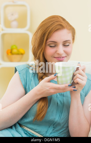 Smiling redhead sitting on the couch smelling coffee Stock Photo
