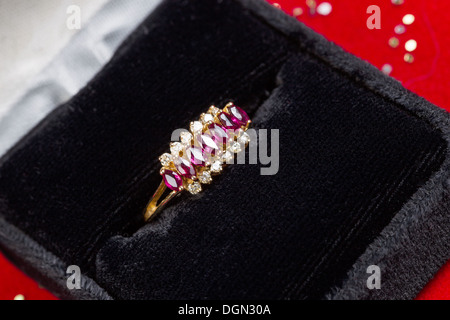 Horizontal photo of gold ring containing precious stones and diamonds sitting inside of Jewelry box on red background Stock Photo