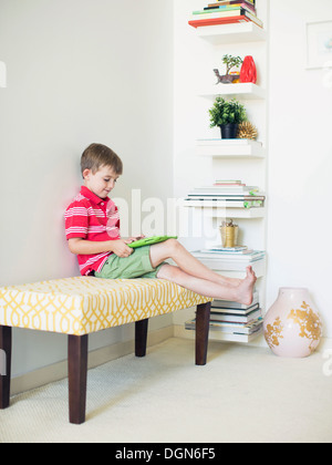 Boy (6-7) sitting on bench using digital tablet Stock Photo