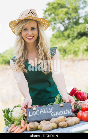 Smiling young female farmer standing at her stall Stock Photo