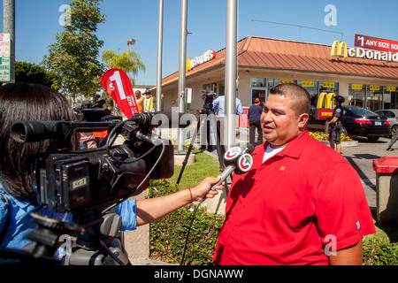 Broadcast journalist interviews Hispanic labor demonstration participant on Los Angeles street has her video cameraman records. Stock Photo