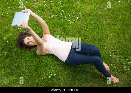 Happy young woman lying on a lawn using her tablet Stock Photo