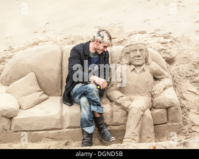 Sculptor creating sand sculpture of a man reclining on a sofa, on River Thames South Bank, London, UK for tips Stock Photo