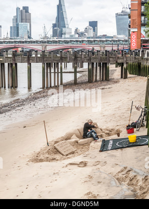 Sculptor creating sand sculpture of a man reclining on a sofa, on River Thames South Bank, London, UK for tips Stock Photo