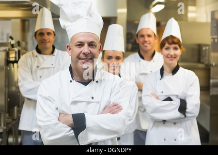Five chefs wearing uniforms posing in a kitchen Stock Photo