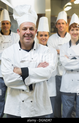 Five chefs wearing uniforms while posing in a kitchen Stock Photo